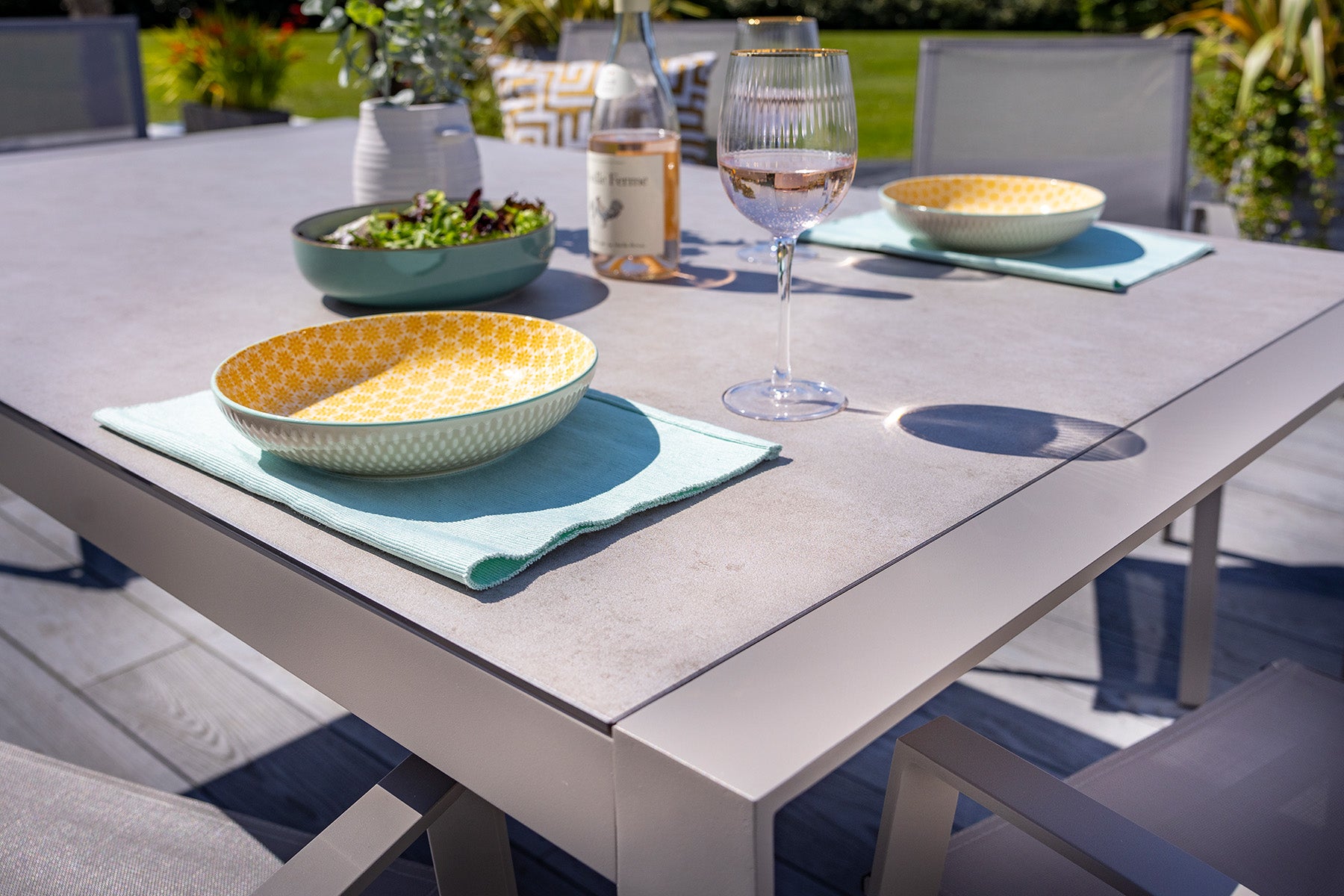 Outdoor dining table with plates, glasses, and a bottle of wine on a patio.