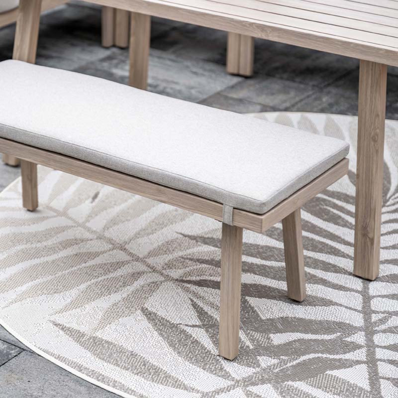 Wooden bench with a white cushion on a patio with a patterned rug.