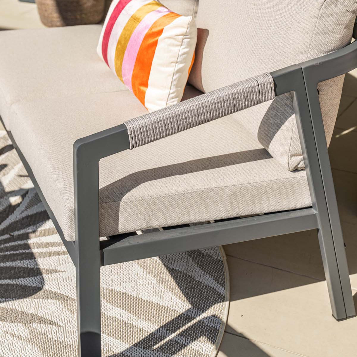 Outdoor patio chair with beige cushions and a colorful striped pillow, surrounded by plants.