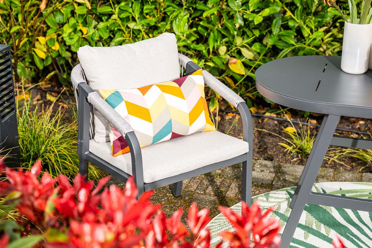 Outdoor furniture set with a chair, table, and colorful pillow against a natural background.