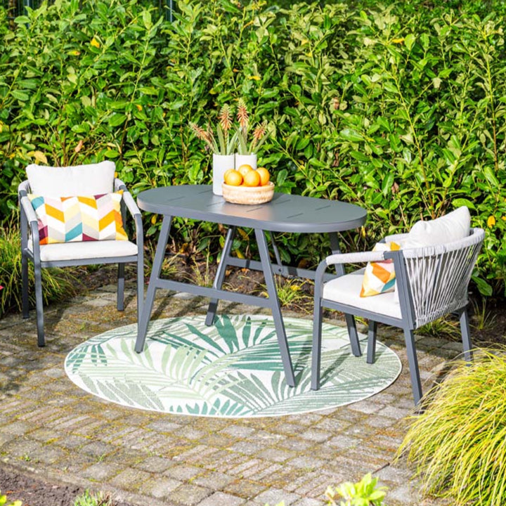 Outdoor patio set with table, chairs, and decorative rug in a garden setting