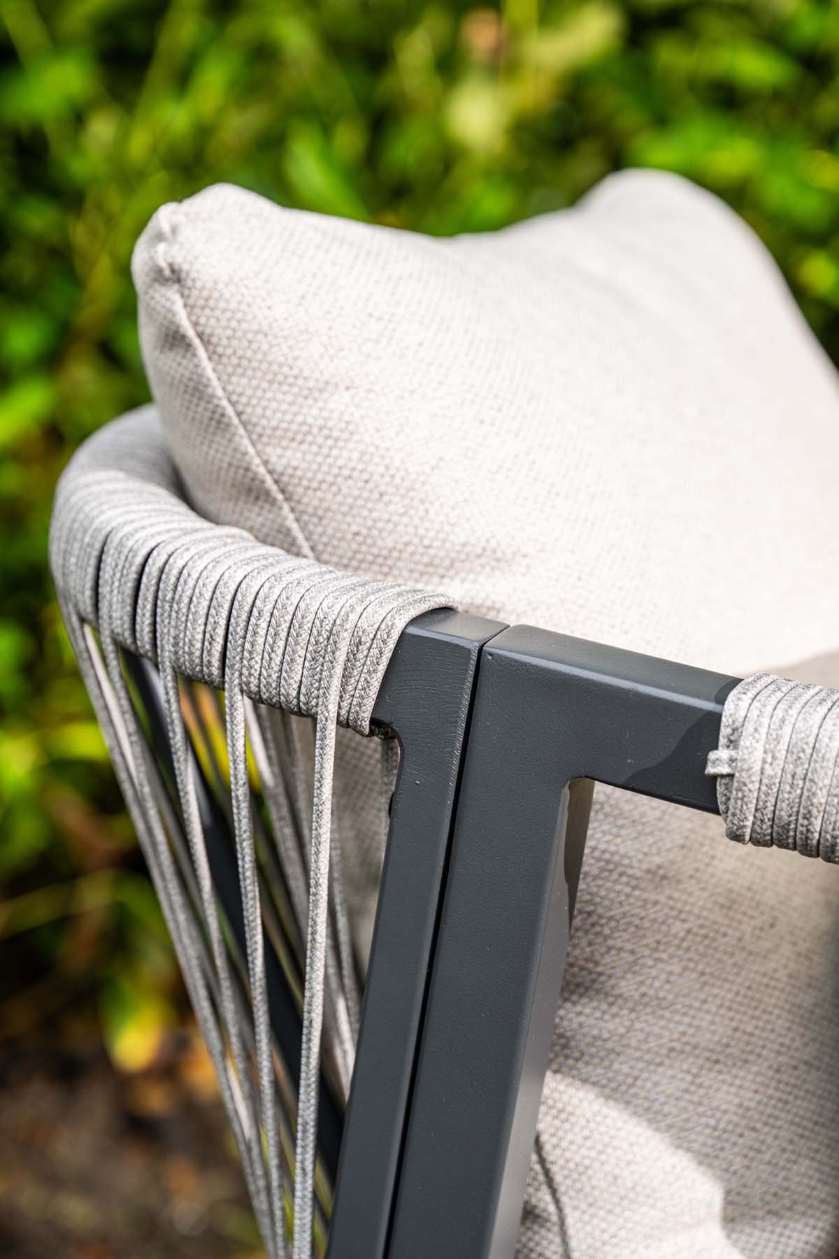 Close-up of a chair with gray cushion and metal frame against a blurred green background