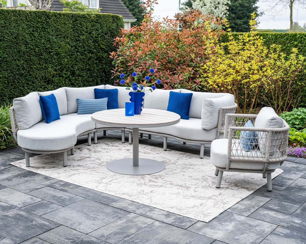 Outdoor patio with gray sectional sofa, round table, and chairs on a paved area.