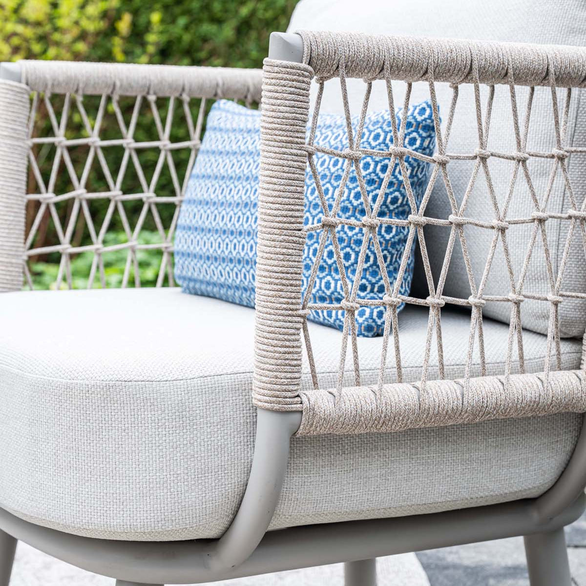 Outdoor chair with woven backrest and white cushion featuring a blue patterned pillow.