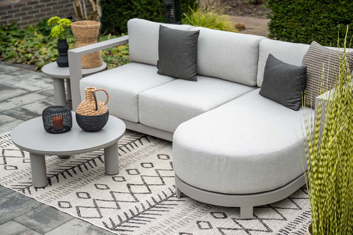Outdoor patio set with a sectional sofa, coffee table, and decorative items on a patterned rug.