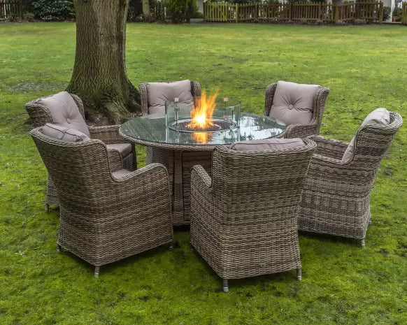 Garden setting with wicker chairs around a fire pit table on grass.