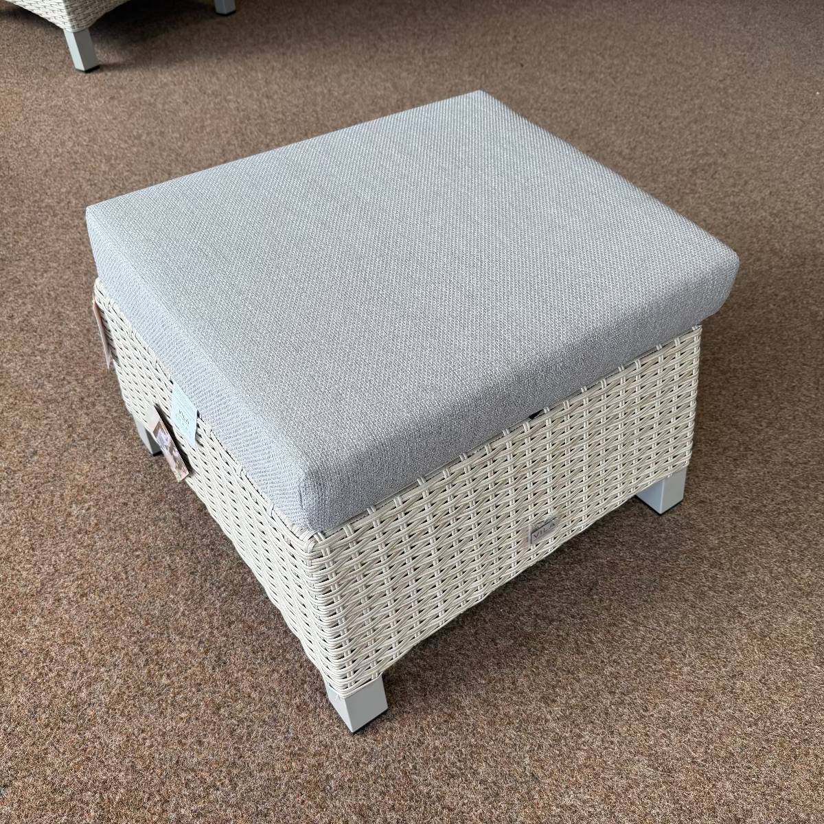 Wicker ottoman with a gray cushion on a carpeted floor