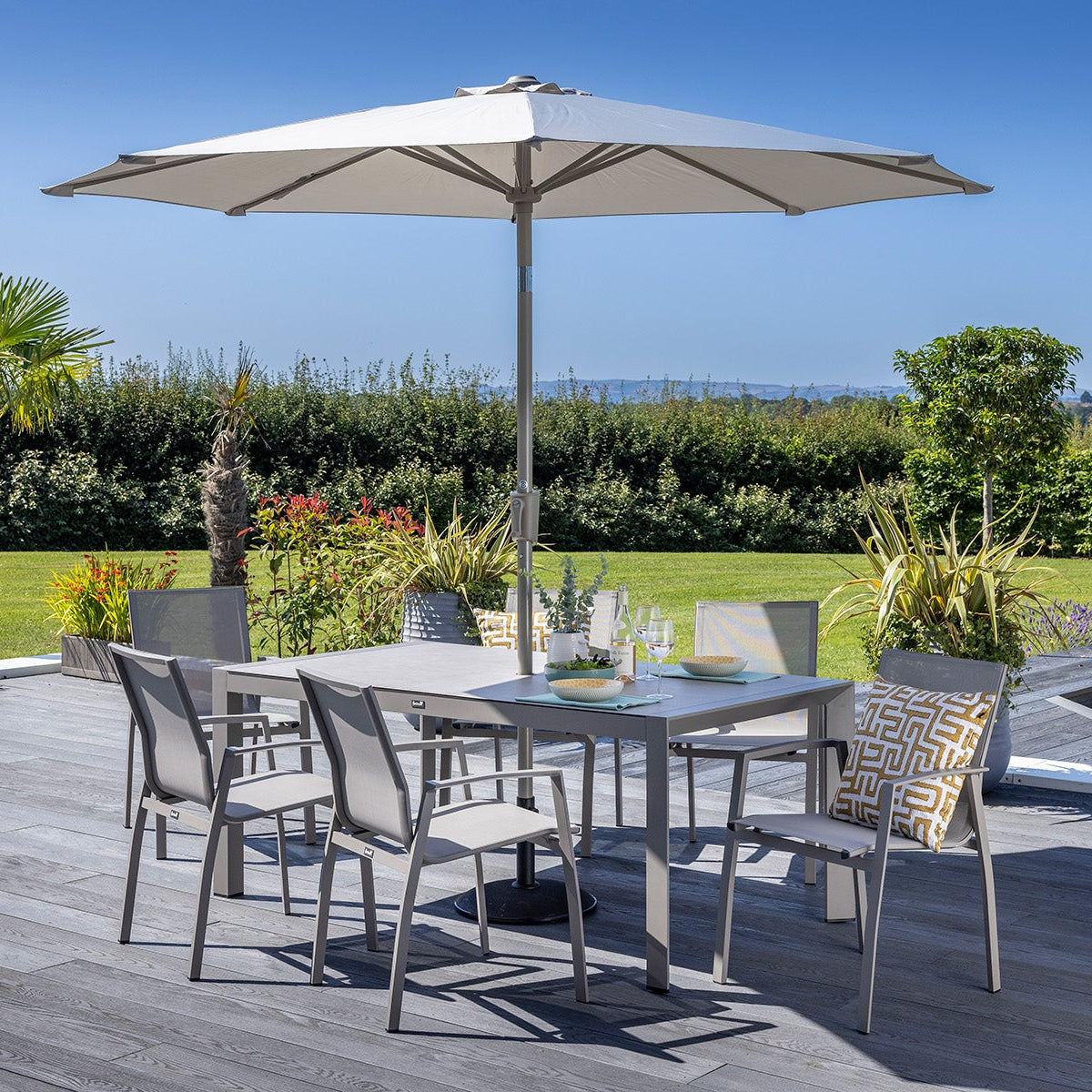 Outdoor dining set with table, chairs, and umbrella on a wooden deck with a scenic background.